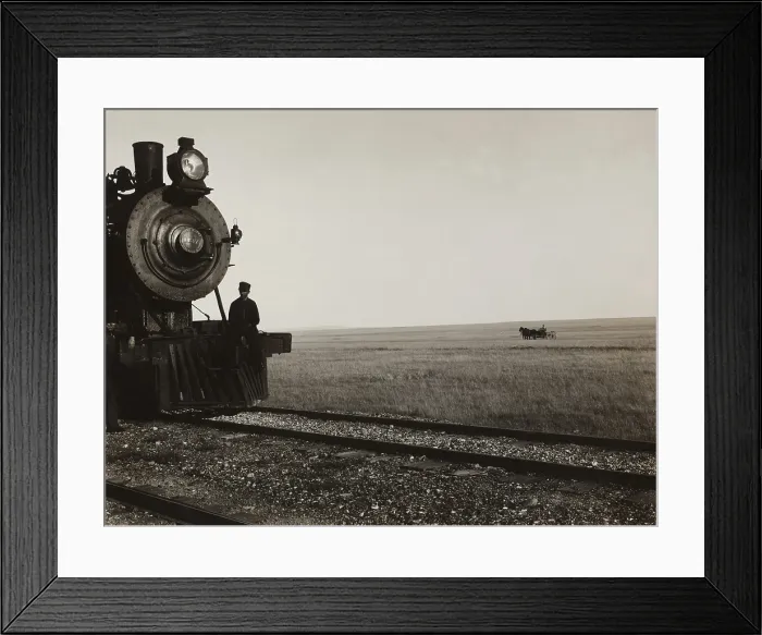 Framed Print : Two men standing on the cow-catcher of a Great Northern Railroad locomotive on the Montana prairie. In the grassy background is a horse-drawn carriage. Ca. 1910