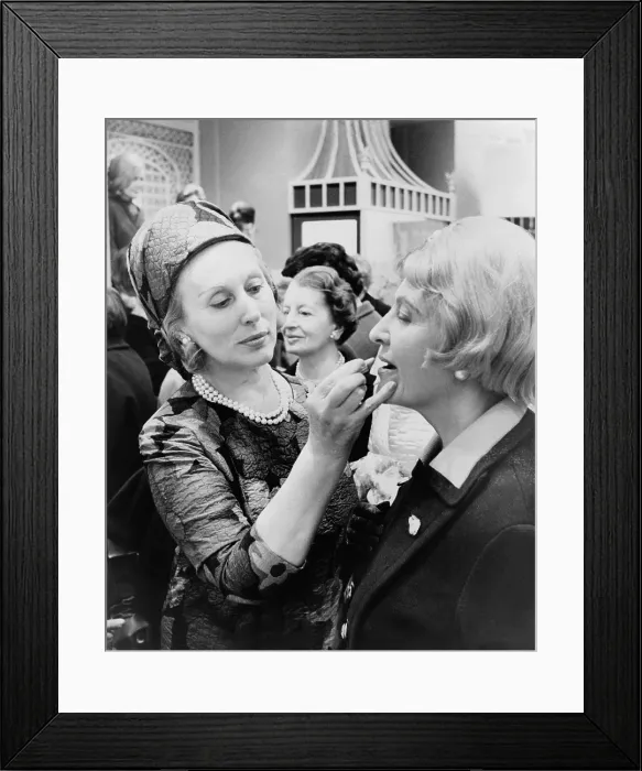 Framed Print : Estee Lauder 1906-2004 cosmetics business leader dressed in an Yves Saint Laurent dress applies lipstick to a customer in New York City. 1966. (BSLOC_2010_18_158) Framed Print : Estee Lauder 1906-2004 cosmetics business leader dressed in an Yves Saint Laurent dress applies lipstick to a customer in New York City. 1966. (BSLOC_2010_18_158)