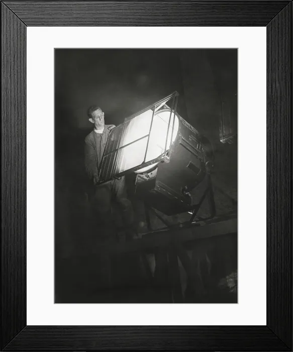 Framed Print : Film engineer using the Dunning Method. He places blue light filter on a special light which will illuminate the filming background