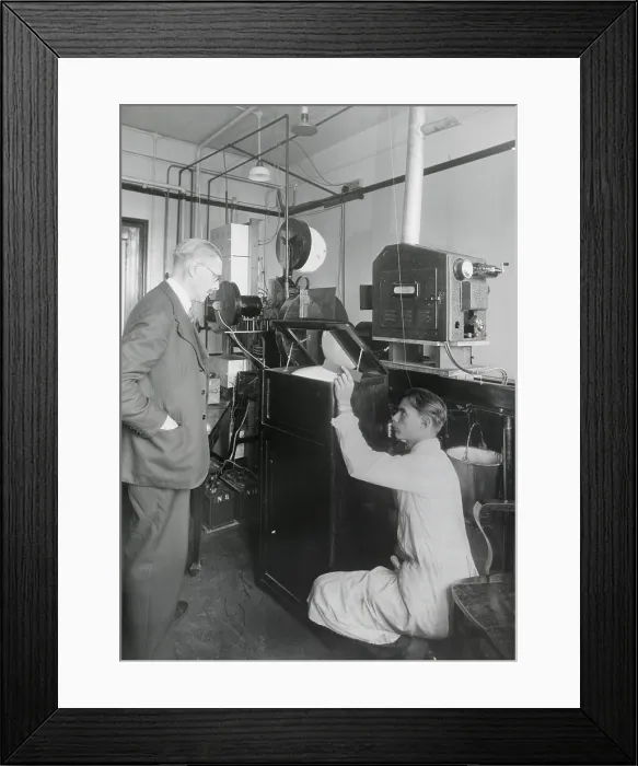 Framed Print : Early television with a viewing mirror that reflects the image of an encased picture tube. In the background is the camera and transmission devices. Ca. 1930