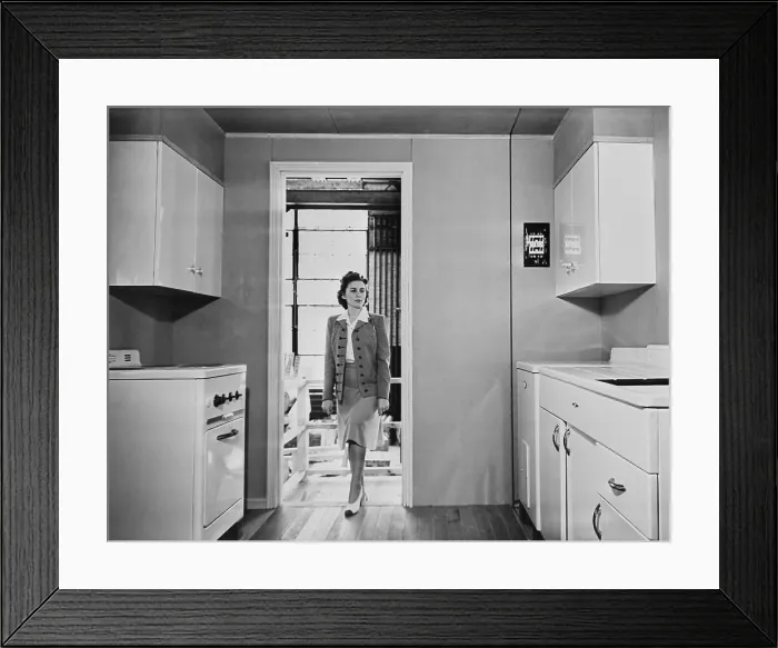 Framed Print : Women enters a modern 1940s kitchen with white enameled metal cabinets. The housing was built by the government for workers on TVA and other Defense projects in World War II