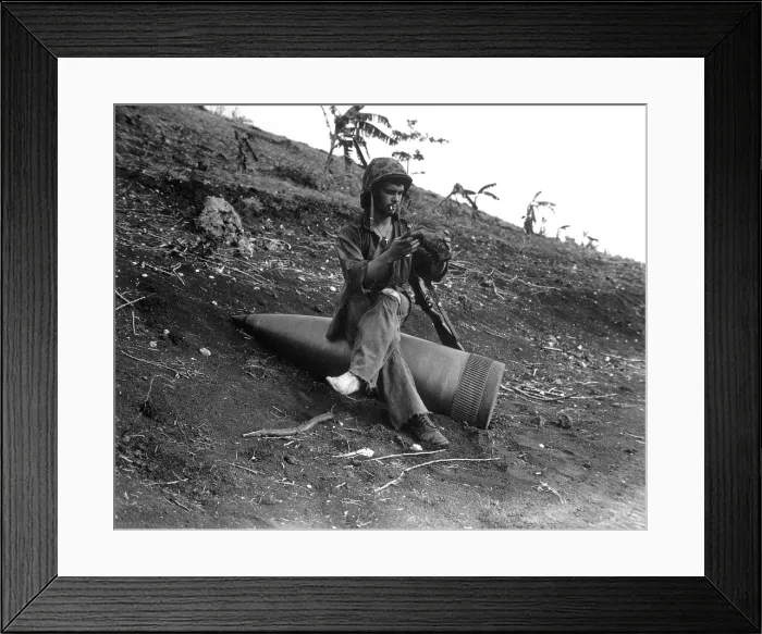 Framed Print : A Marine sits on an 16-inch naval shell to shake a three-days of sand from his boots. Battle of Saipan battle against the Japanese during World War 2. July 4, 1944