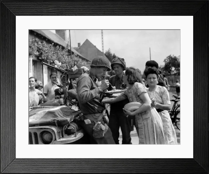 Framed Print : Three U.S. soldiers eat on homemade food on plates prepared by a French woman in Summer 1944. The liberated civilians also decorated their jeep with flowers
