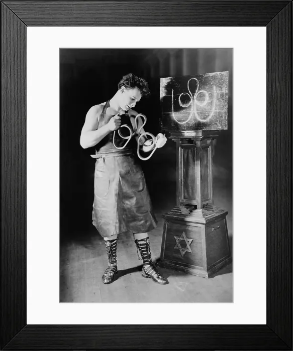 Framed Print : Sigmund Zishe Breitbar, in his blacksmith costume as he bends an iron bar into a trefoil. Ca. 1924