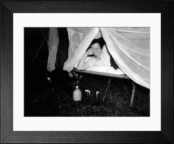 Framed Print : American WAC raises the netting over her cot as a photographer's flash illuminates the scene. On the ground are her water bottle and boots. Normandy, France, 1944