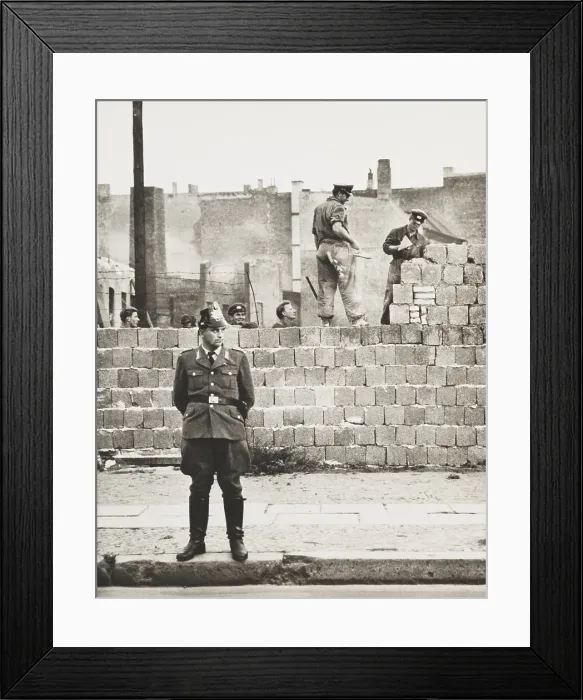 Framed Print : West Berlin policeman stands before the concrete block wall dividing East and West Berlin