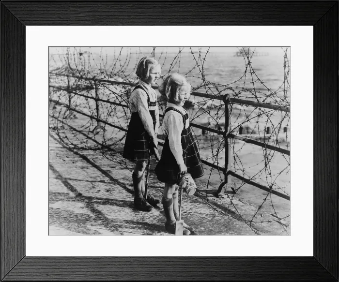 Framed Print : Two girls on the south coast of England look out to the beach through a barbed wire fence in 1940