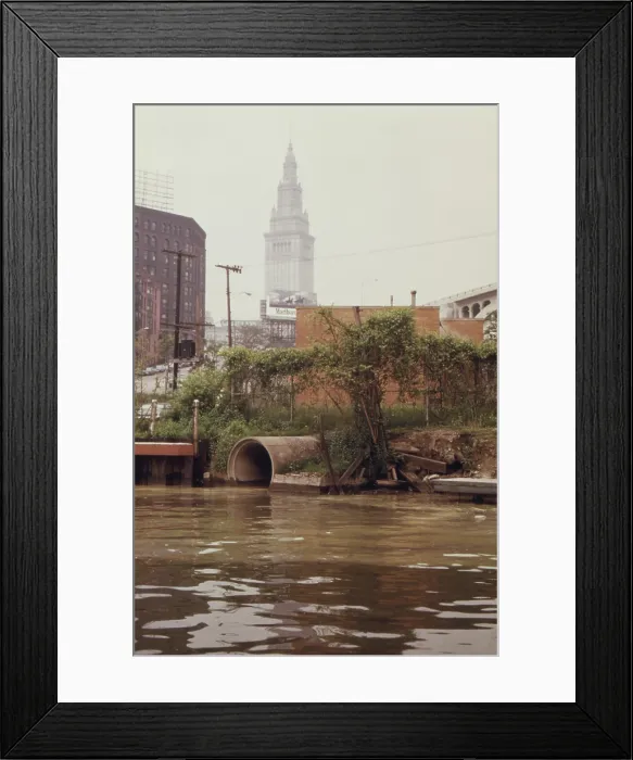 Framed Print : A Cleveland city pump station discharges sewage into the Cuyahoga River. In the background is the Terminal Tower a landmark skyscraper in downtown Cleveland. Ca. 1973-75
