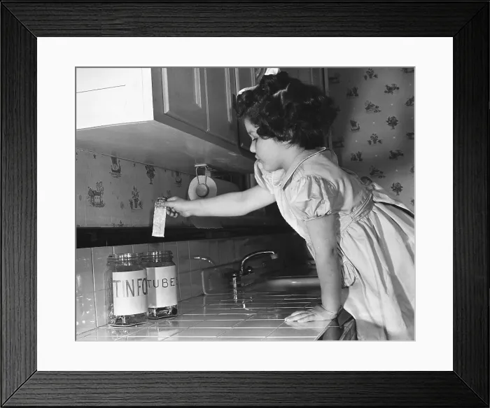 Framed Print : A little girl deposits a tooth paste tube in a household collection jar during World War 2. Vital tin and alloy metals were recycled. Ca. 1942-45. (BSLOC_2013_14_179)