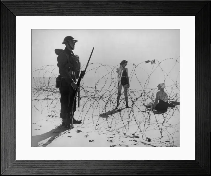 Framed Print : Soldier standing guard next to barbed wire barricade on an English beach during World War 2. On the other side are two British women in bathing suits. Sept. 21, 1940