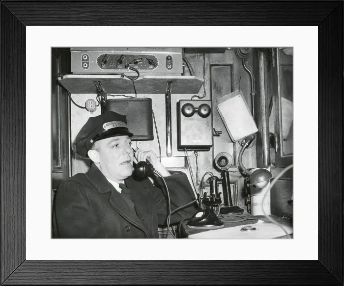 Framed Print : Railroad conductor uses an on board telephone to communicate with other parts of the train. Ca. 1930's - (BSLOC_2015_1_231)
