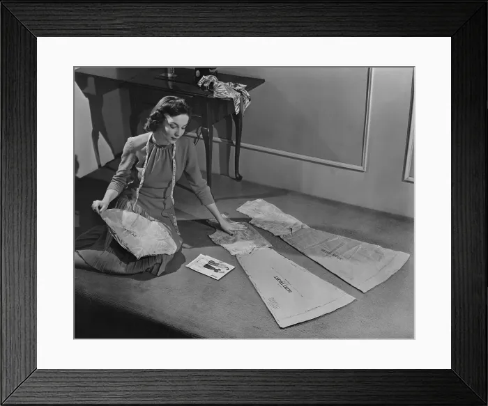 Framed Print : In the 1940s, many women continued to sew their own clothing. Fashionable patterns were distributed nationwide. In the background is a contemporary Singer Sewing machine. 1943