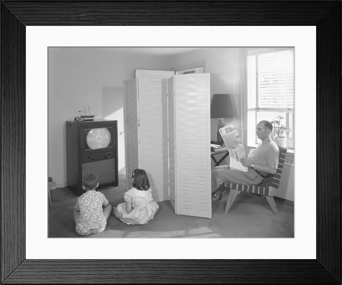 Framed Print : Father reading newspaper, while two children anticipate the start of television programming