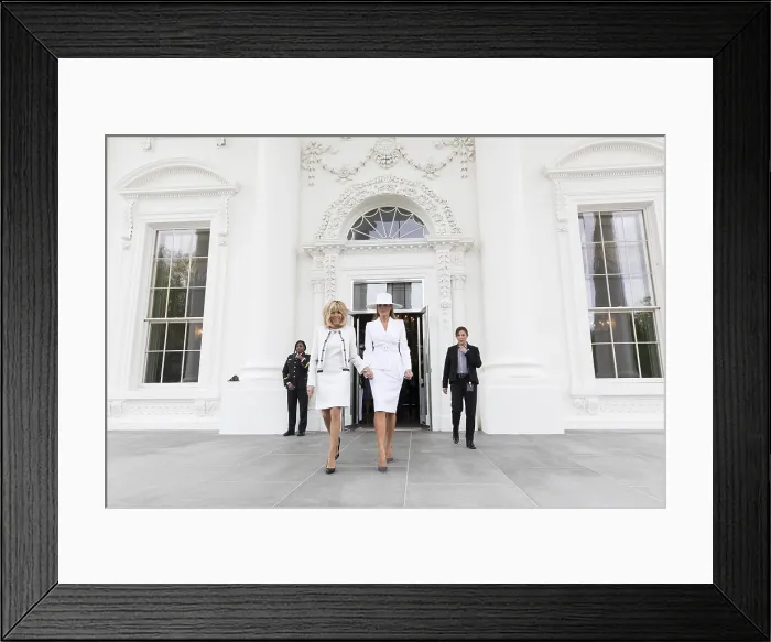 Framed Print : First Ladies Melania Trump and Brigitte Macron at the official arrival ceremony for the President of France. Melania wears a Michael Kors white suite, with a hat by Herv Pierre