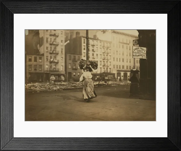 Framed Print : Italian woman carrying heavy bundle of clothing on her head Near Astor Place, New York City. She will sew the garments at home for low wages