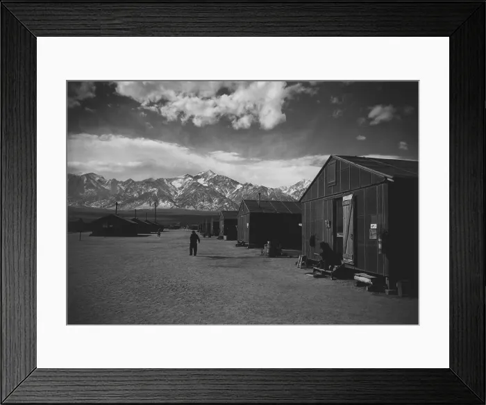 Framed Print : Manzanar Relocation Center, a World War II internment camp for Japanese Americans. A lone man walks on a barracks lined street in the winter of 1943. Photograph by Ansel Adams