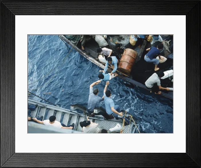 Framed Print : Assistance to Boat People, in a small craft on South China Sea, April 3, 1975. Crewmen of the amphibious cargo ship USS Durham take on Vietnamese refugees