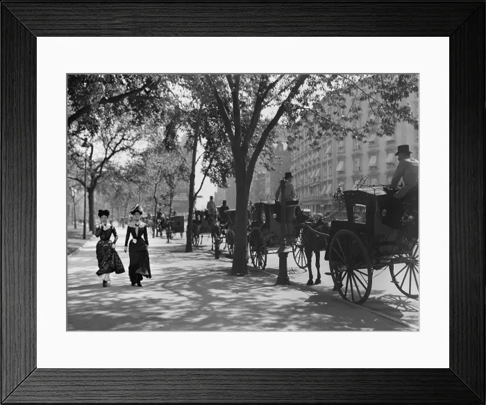 Framed Print : Two young women in fashionable cinched waist dresses, walk on the Madison Avenue sidewalk, NYC. They pass a line of horse drawn cabs, waiting for hire. Photo by Byron, c