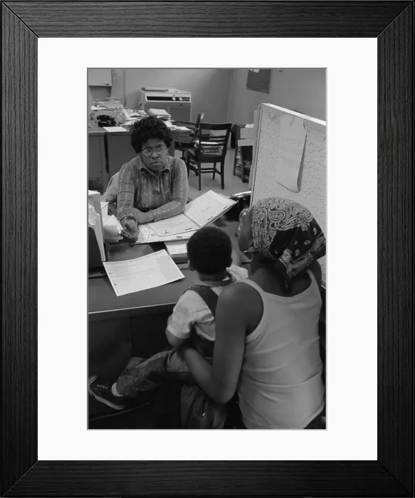 Framed Print : An African American woman with a child on her lap talking to a case worker at a New York City welfare office. May 14 1976 Framed Print : An African American woman with a child on her lap talking to a case worker at a New York City welfare office. May 14 1976