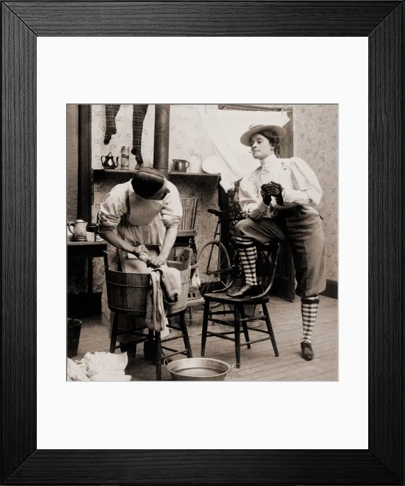 Framed Print : Humorous scene of life with the new woman. Woman smoking and wearing knickers postures arrogantly as a man drudges over laundry. 1901