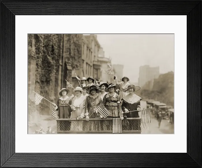 Framed Print : Smiling young women waving flags from the top of an open vehicle in a New York City parade. Ca. 1910-1915