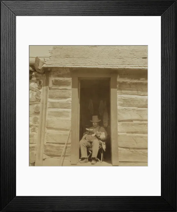 Framed Print : President Theodore Roosevelt reading in the doorway of West Divide Creek Ranch House. In his lap is the hunting dog Skip he adopted and took back to Washington