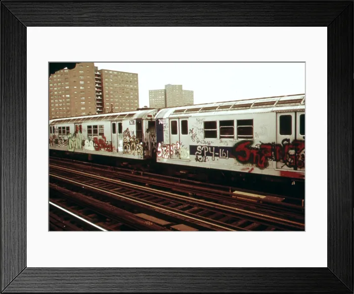 Framed Print : New York City Subway. A graffiti painted subway train with housing projects in the background. Outside of Manhattan many New York subways run on elevated tracks. May 1973