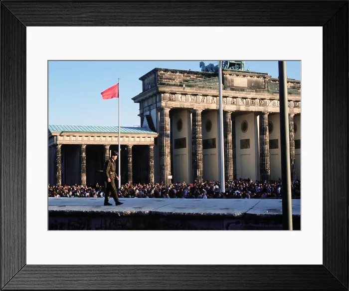 Framed Print : Crowds of Berliners around the Brandenburg Gate following the structure's official opening on Dec. 22 1989. In the foreground an East German guard walks on the Berlin Wall
