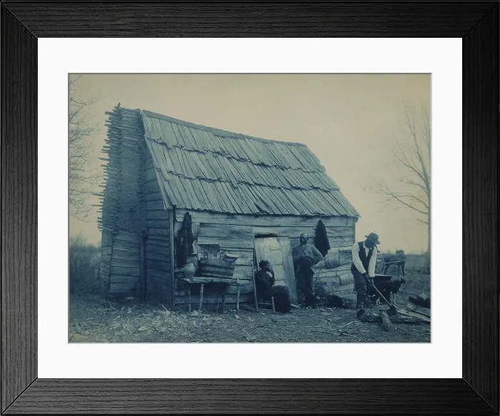 Framed Print : African American man chops wood outside a cabin, presumably the home of the middle aged couple nearby. The tree is bear of leaves, and fire wood will be needed Framed Print : African American man chops wood outside a cabin, presumably the home of the middle aged couple nearby. The tree is bear of leaves, and fire wood will be needed