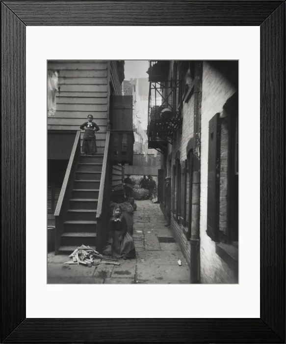 Framed Print : BAXTER STREET ALLEY, RAG PICKERS ROW, by Jacob Riis, 1888-89. Two young girls pose near their flats, while five men stand in the alley, near rough bundles