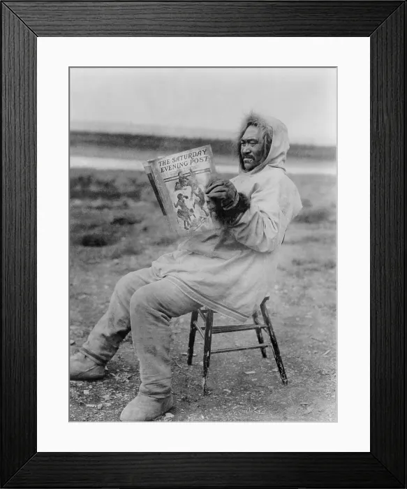 Framed Print : Eskimo man reading Saturday Evening Post in the Arctic region, 1913. Seated on a chair outdoors, he holds a library set of 1913 issues in a staged photo