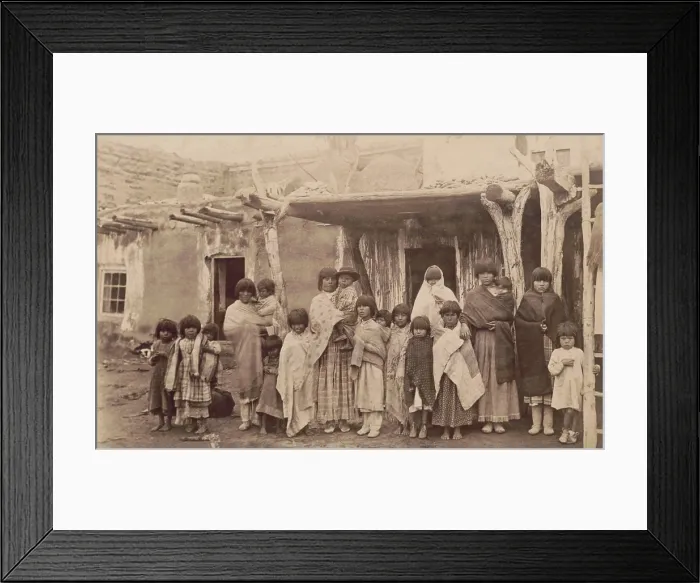 Framed Print : A group portrait photograph of nineteen women and children at Tesuqua Pueblo, ca. 1890-1900. The post and beam supports of the Pueblo architecture are evident