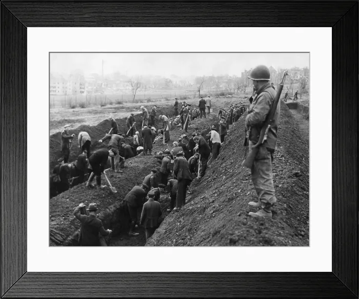 Framed Print : U.S. Soldier guards the reburial of concentration camp victims by German civilians. Ca. April-May 1945. Unidentified location in Germany, World War 2 (BSLOC_2015_13_23)
