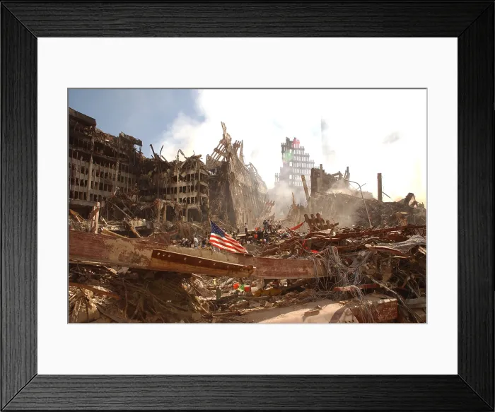 Framed Print : Smoke rises from the World Trade Center's collapsed North Tower. On the left are the remains of a lower structure, WTC 6. A large flag is secured to a beam in the foreground Framed Print : Smoke rises from the World Trade Center's collapsed North Tower. On the left are the remains of a lower structure, WTC 6. A large flag is secured to a beam in the foreground