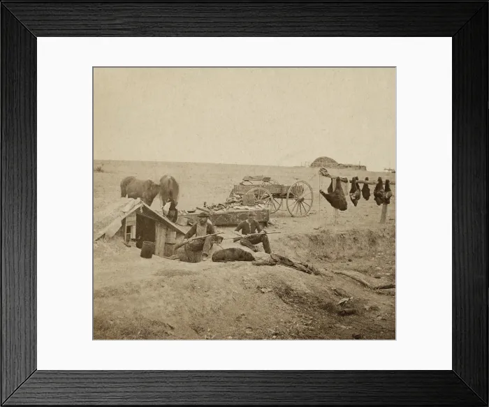 Framed Print : Buffalo hunters dugout home and encampment, ca. 1870. The two hunters pose with their rifles and dog. Unskinned bison meat hangs at right
