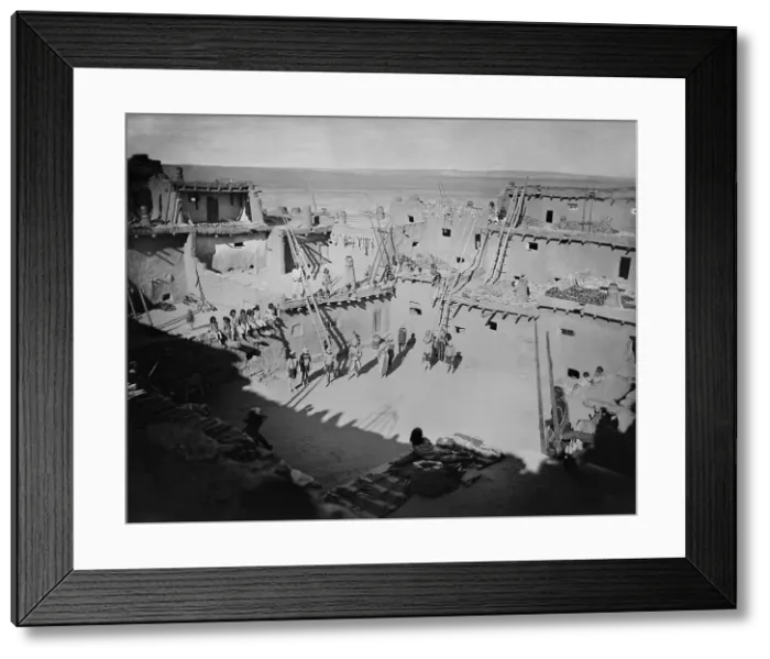 Framed Print : Native American spectators sit on an upper terrace, about to watch the Masked Mud Heads dance in a courtyard of the Zuni Pueblo. 1879 photo by John K