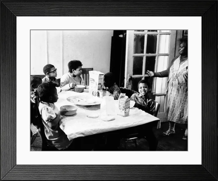 Framed Print : An African American mother serves six children a breakfast of corn flakes and milk in their apartment in New York's Harlem district Framed Print : An African American mother serves six children a breakfast of corn flakes and milk in their apartment in New York's Harlem district