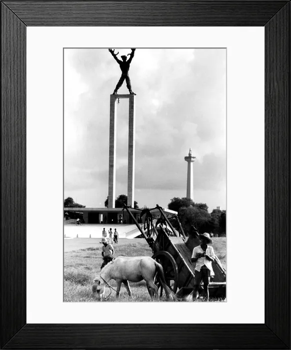 Framed Print : Two of Djakarta's expensive symbols: The Figure Breaking Chains, which glorifies the take-over of West Irian from the Dutch, and The National Monument