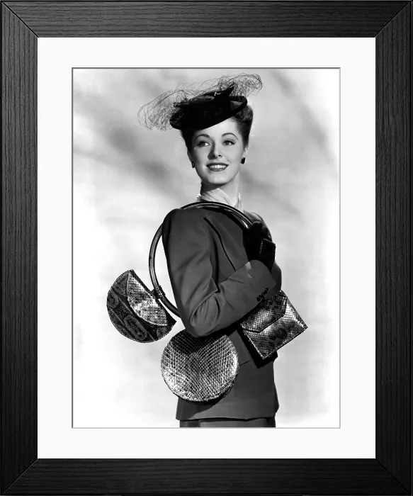Framed Print : ELEANOR PARKER carrying 3 small handbags of blueberry red reptile and an over the shoulder hoop of plastic. 1945