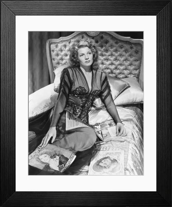 Framed Print : Rita Hayworth sitting on a bed with movie magazines featuring her image on the cover, ca. 1942
