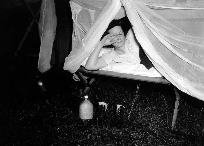 Framed Print : American WAC raises the netting over her cot as a photographer's flash illuminates the scene. On the ground are her water bottle and boots. Normandy, France, 1944