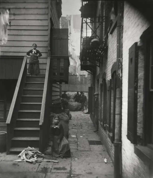 Framed Print : BAXTER STREET ALLEY, RAG PICKERS ROW, by Jacob Riis, 1888-89. Two young girls pose near their flats, while five men stand in the alley, near rough bundles