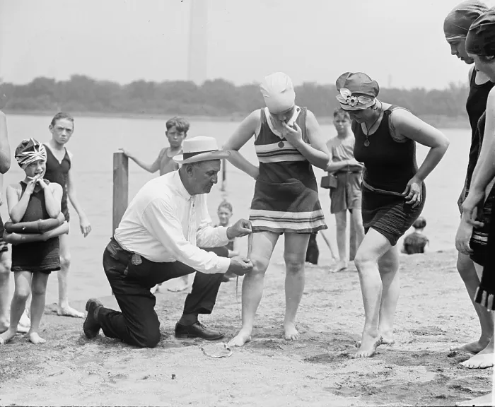 Framed Print : A beach official checks the amount of thigh exposed by a young ladies bathing suit in 1922. The hemlines on all women's clothing reached new heights in the 1920's