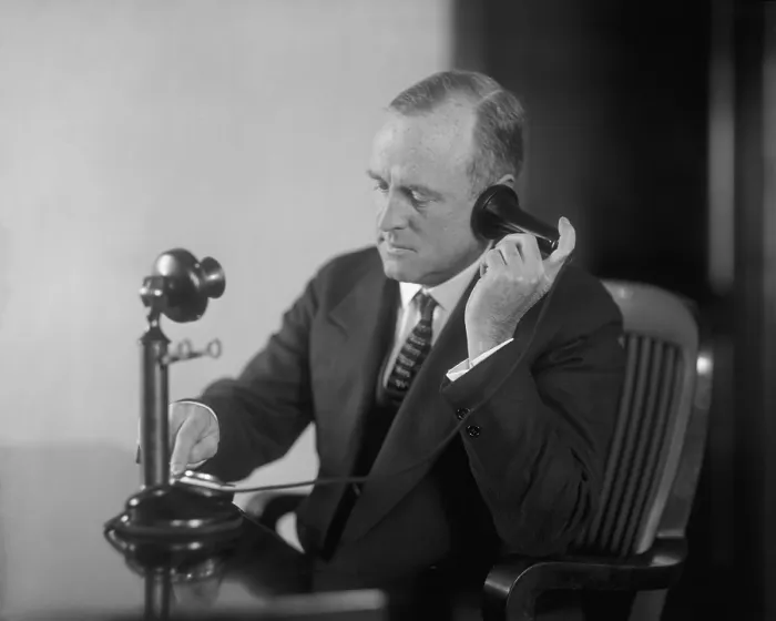 Framed Print : Businessman dialing an early 20th century desk phone with separate ear receiver and mouth transmitter. Ca. 1920