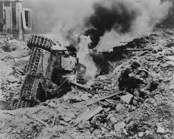 Framed Print : Canadian soldier is attended by a medic near Falaise, France. A burning overturned German tank is the in rubble nearby, during the Battle of the Falaise Pocket