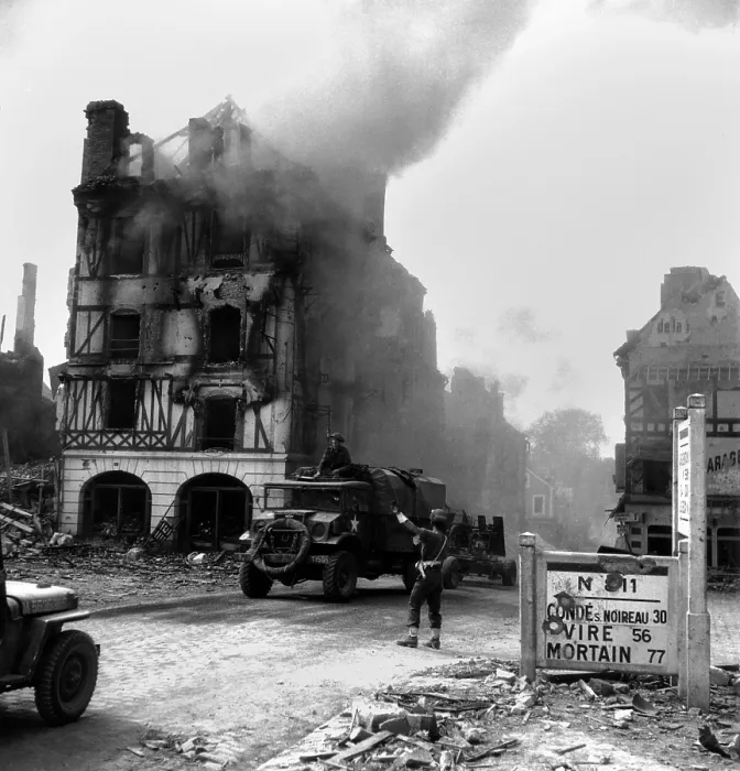 Framed Print : Canadian soldier controls traffic in burning Falaise ruins on August 17, 1944. A truck towing an anti-aircraft gun drives toward the Falaise Pocket. Normandy, France, World War 2