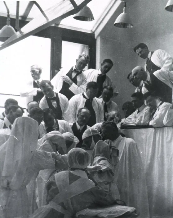 Framed Print : Charles H. Mayo (1865-1939), at center right in surgical gown, cap, and mask, in an operating amphitheatre assisted by four nurses and observed by others in the gallery