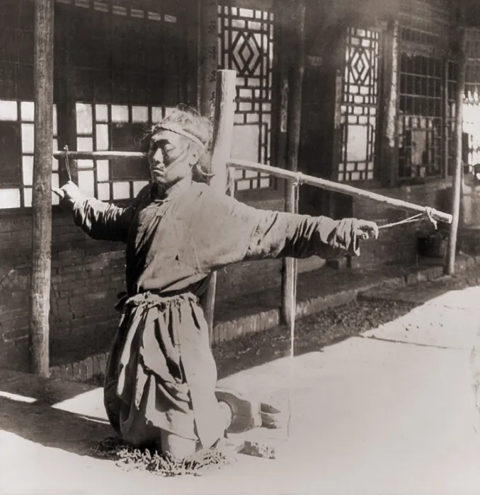 Framed Print : Chinese prisoner kneeling on chains, with his ankles in stocks, while his arms are tied by the thumbs to a pole supporting his arms. Moukden, China. Circa. 1900 Framed Print : Chinese prisoner kneeling on chains, with his ankles in stocks, while his arms are tied by the thumbs to a pole supporting his arms. Moukden, China. Circa. 1900