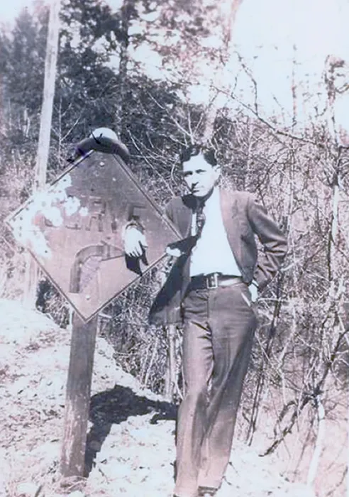 Framed Print : Clyde Barrow (1909-1934) dressed in a suit and standing with his hand place through a hold on a road sign Framed Print : Clyde Barrow (1909-1934) dressed in a suit and standing with his hand place through a hold on a road sign