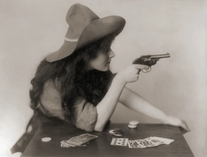 Framed Print : Cowgirl with deck of cards and chips, pointing a pistol. 1912